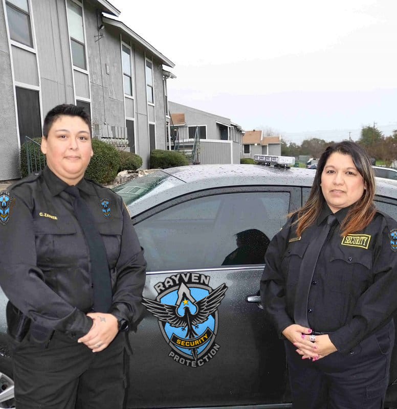 Two security officers standing next to Rayven Security Protection Private Security vehicle in front of a building, providing safety services.