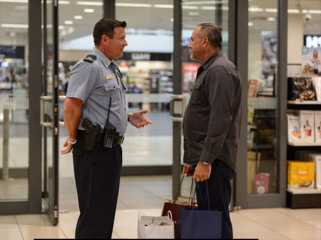 Security guard calmly speaking with a shopper near a retail store exit, illustrating a controlled and procedural detention situation without escalation.