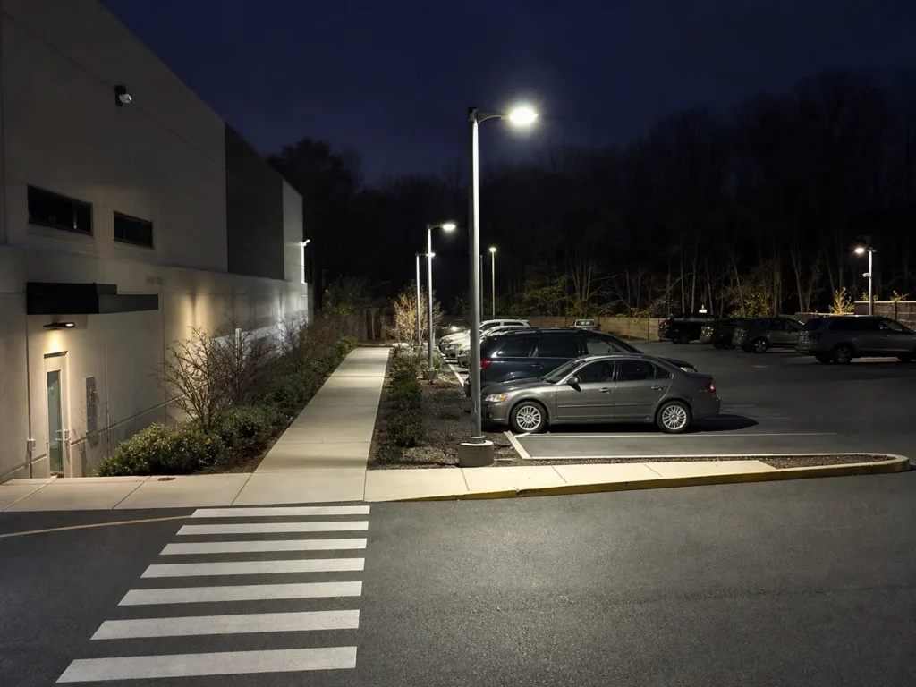 Well-lit commercial parking lot at night with visible walkways, parked cars, and exterior building lights